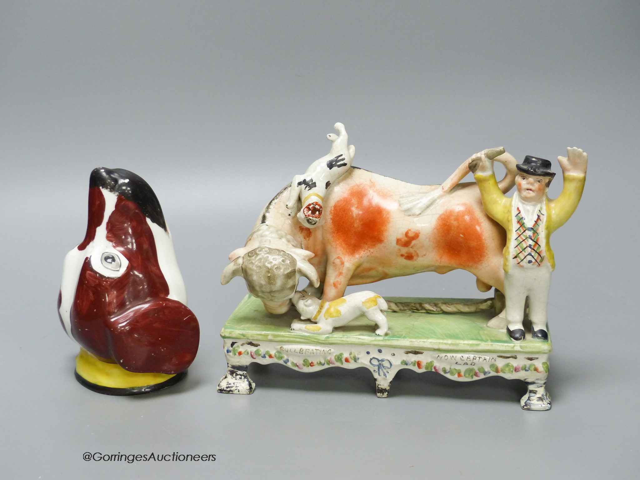 A 19th century Staffordshire bull baiting group, width 19cm, and a 19th century English porcelain spaniel’s head stirrup cup (2)